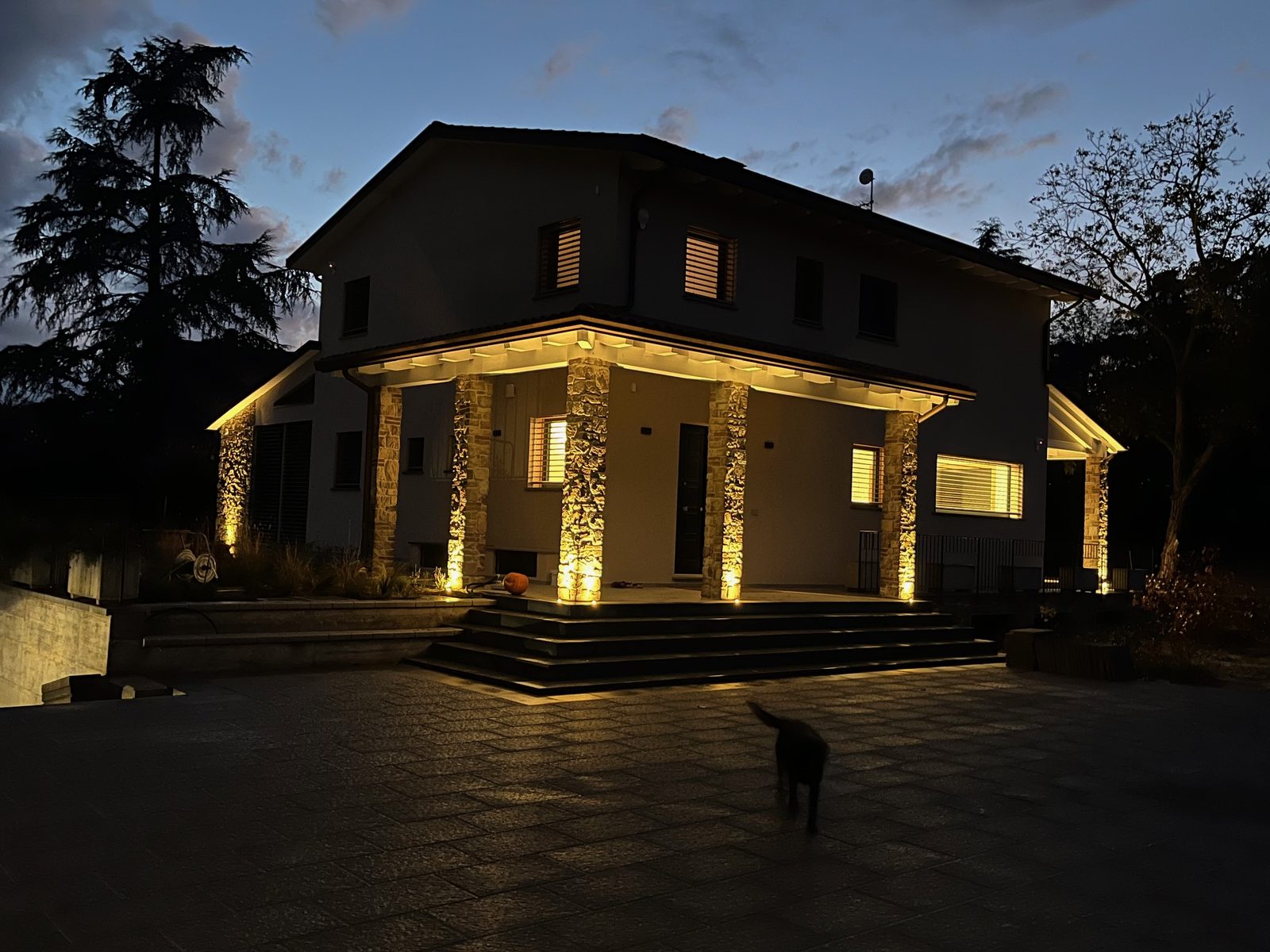 Casa in legno a Deruta la sera, con il portico e i pilastri in pietra illuminati