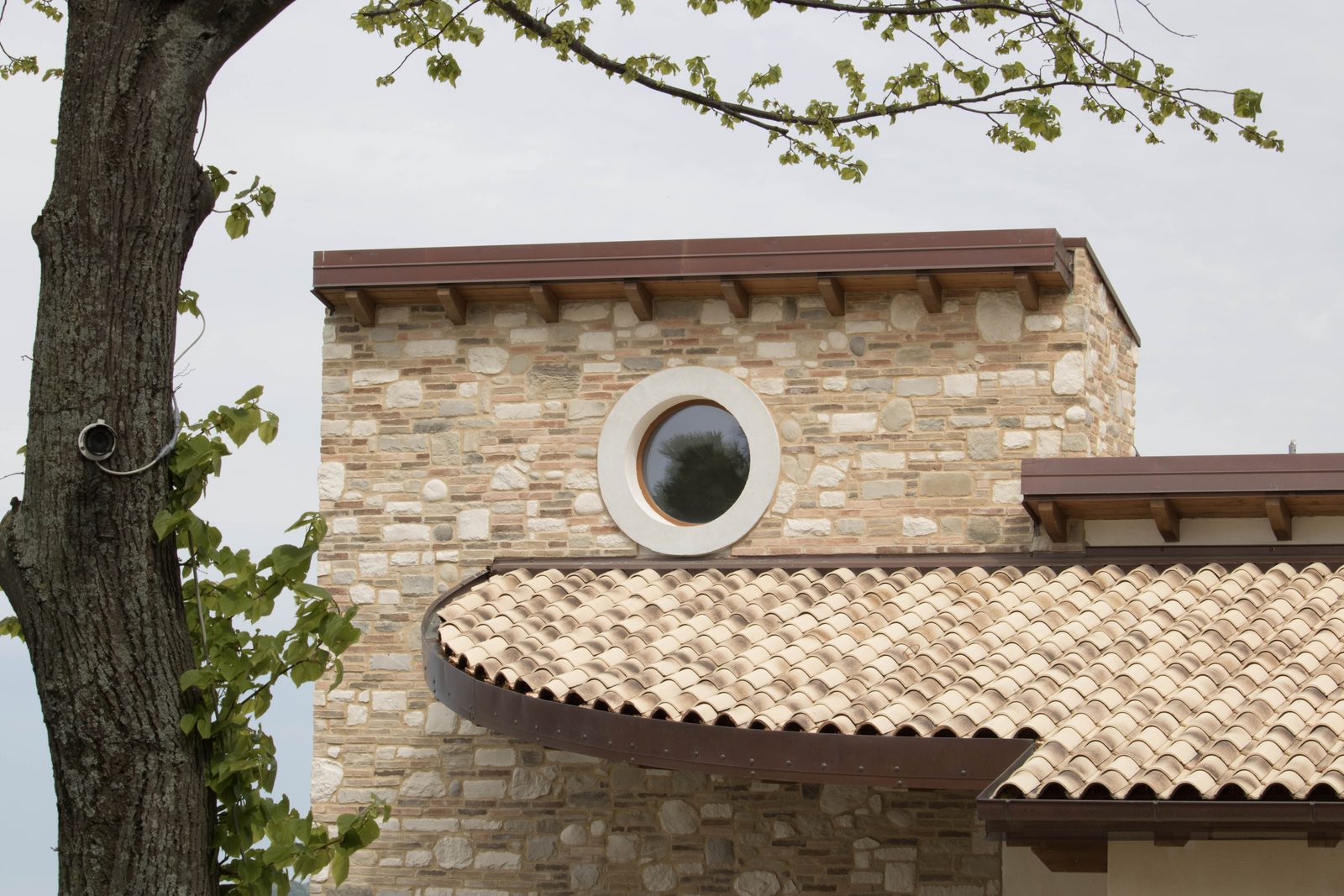 Casa in legno a Monterubbiano con facciata in pietra, oblò rotondo e falda di coppi in curva